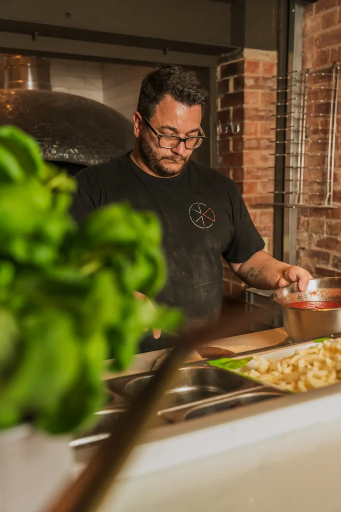 A chef is working at a food station holding a bowl of passata