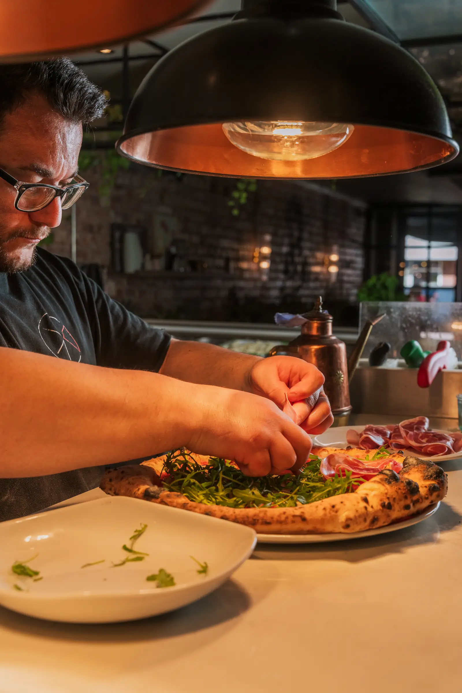 A chef is putting the finishing touches to a pizza under a warm lamp