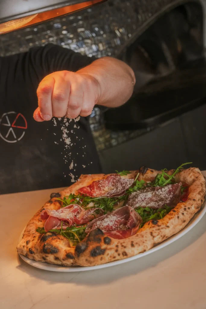 A chef is sprinkling parmesan cheese onto a pizza