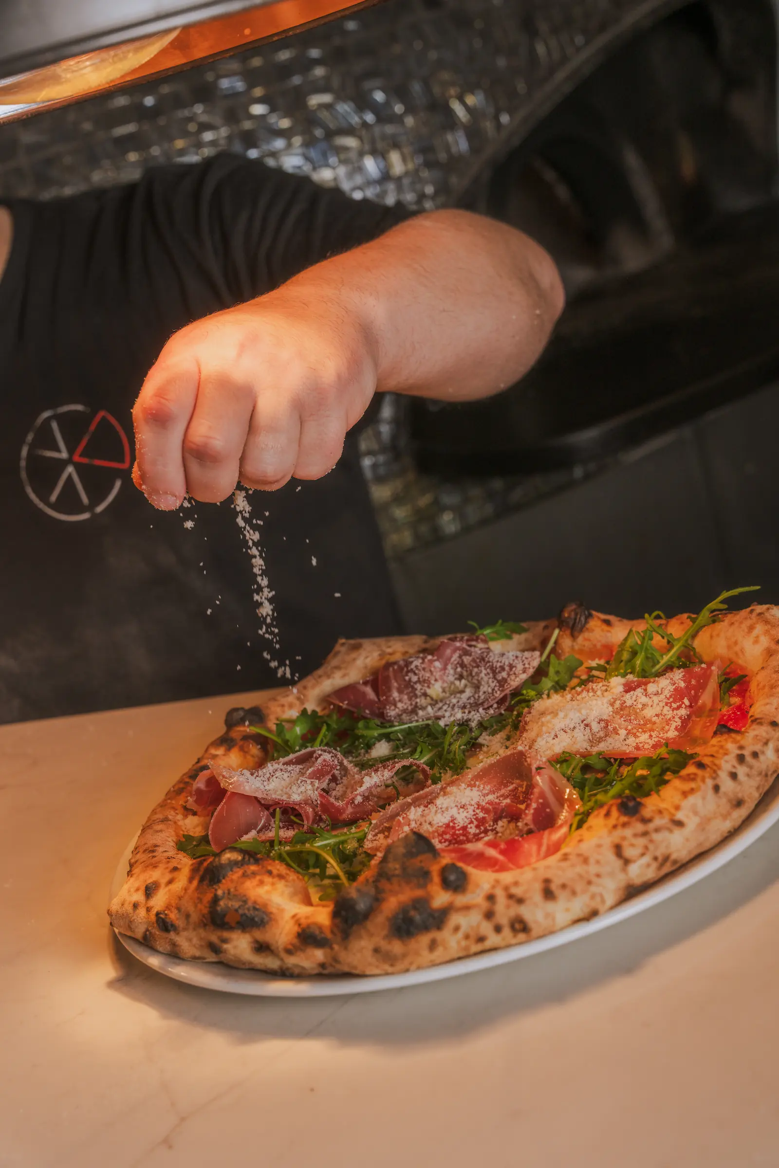 A chef is sprinkling parmesan cheese onto a pizza