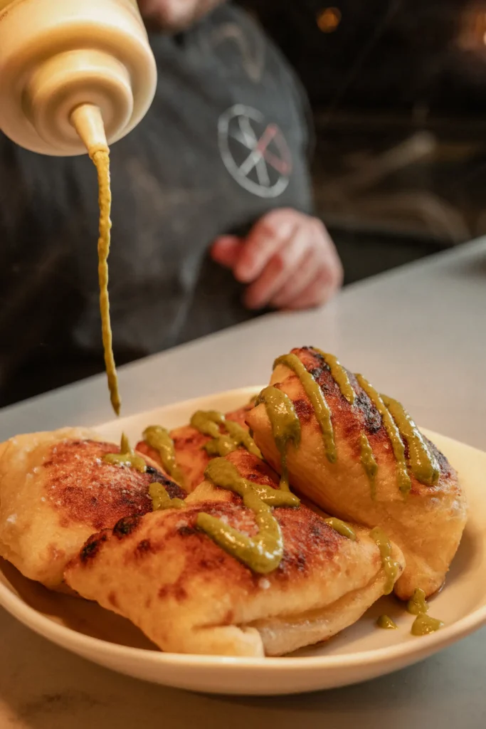A chef is drizzling basil sauce onto cooked panzerotti