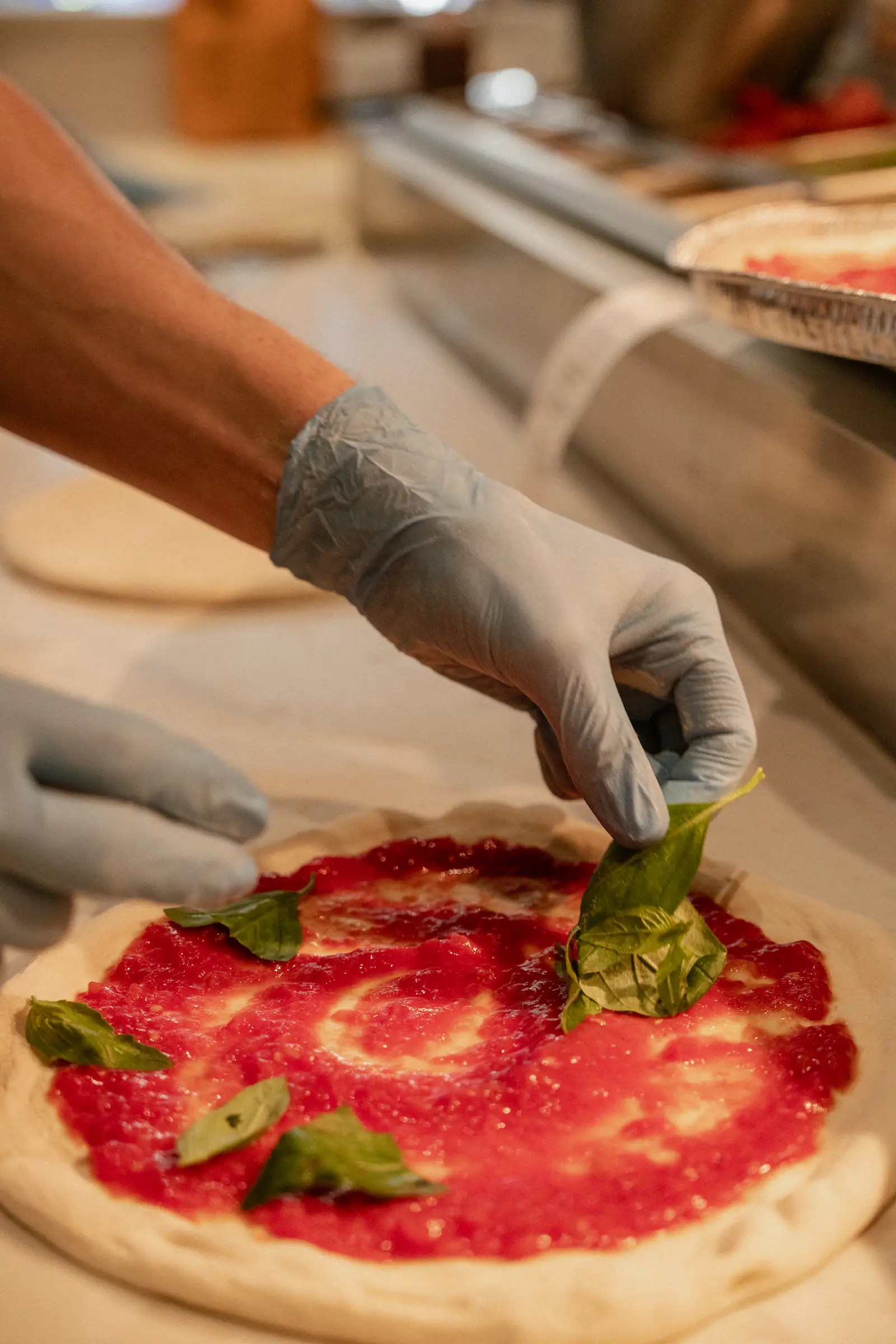 Photo of a chef adding basil leaves to a pizza base.