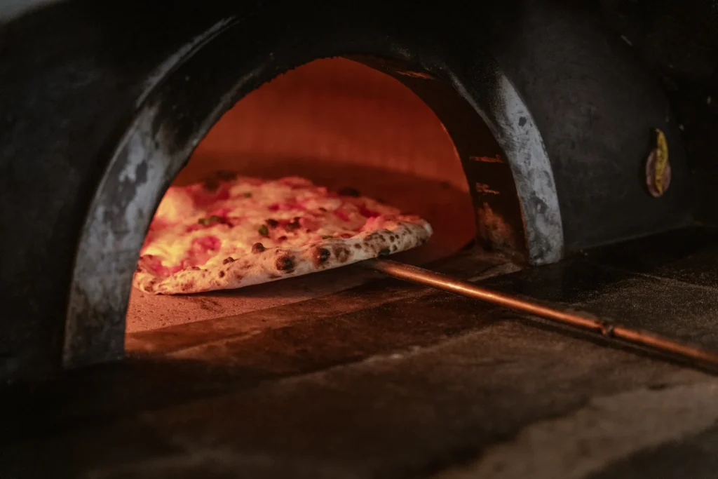 A chef is using a tool to take a cooked pizza from the oven.
