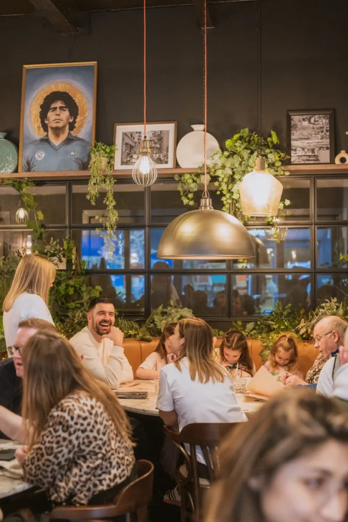Busy restaurant scene with a large group smiling and chatting with a server.
