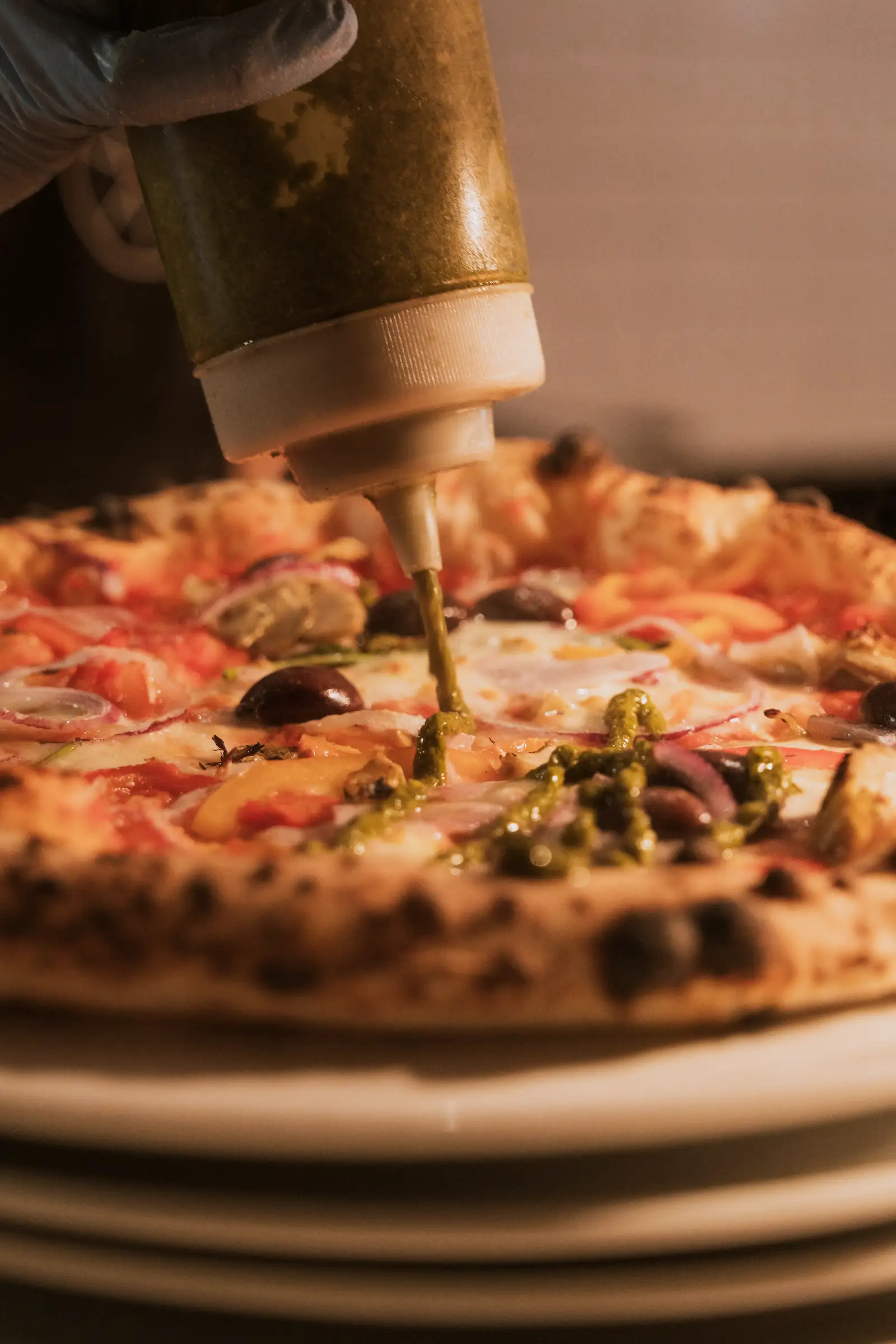 A chef is drizzling basil sauce onto a pizza.