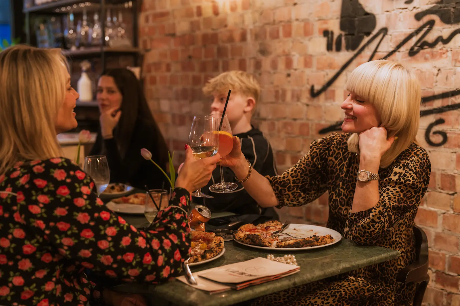 Two women are clinking cocktail glasses midway through a meal