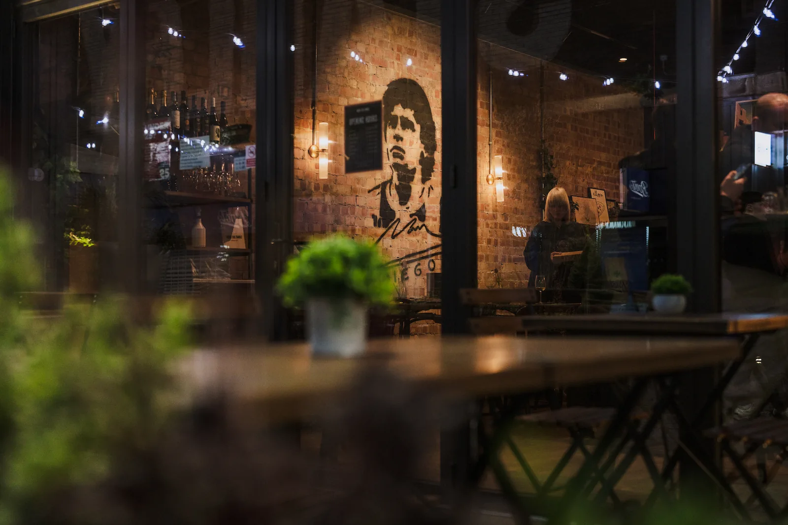 Photo from the restaurant exterior with outside seating and green plants.